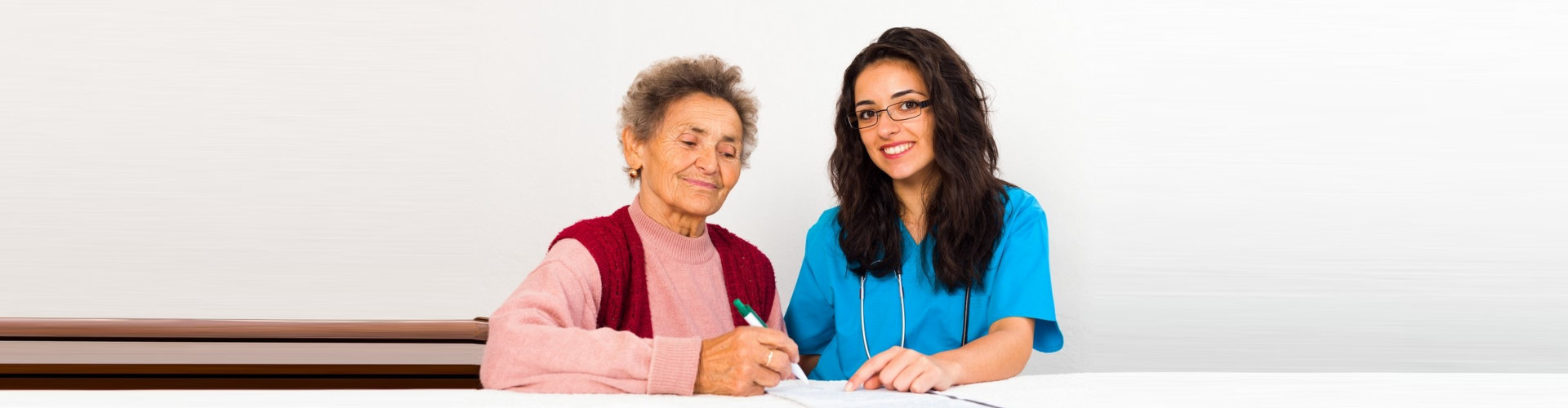 an elderly woman filling out a form with a female caregiver